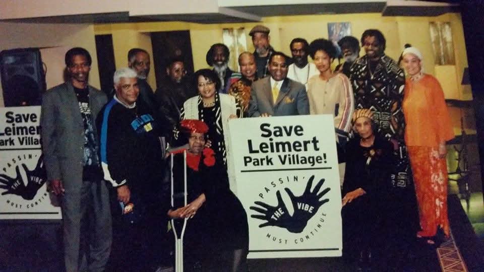Group of people holding a sign that reads 'Save Leimert Park Village' at an indoor event.